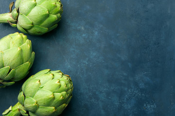 Heap of ripe green artichokes on dark blue background. Creative food poster. Minimalist style. Mediterranean Spanish cuisine healthy plant based diet superfoods concept
