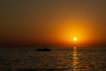 Orange summer sunset on sea with rocks and boat