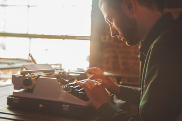 Young male journalist typing on an antique vintage typewriter machine