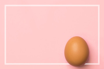 One brown egg on pastel pink background in white frame. Easter concept. Trendy minimalist style. Holiday card poster banner with copy space