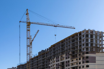 The building of the house. The crane and the new brick building in the clear sunny day on the background of blue sky