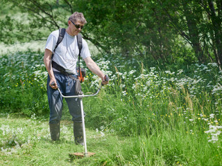 Man is using grass trimmer on his countryside yard. © Artem
