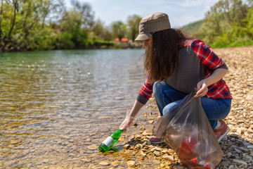 Woman volunteer helps clean the shore of river of garbage. Earth day and environmental improvement...