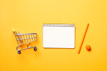 Shopping concept. Budget concept. shopping cart,  blank paper notebook with pen on a yellow background.