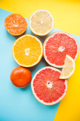 Naklejka na ściany i meble Flat lay of cut ripe juicy grapefruit, lemon and orange on yellow and blue background. Citrus pattern.