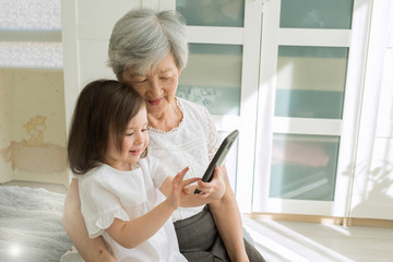 Great-grandmother sits with great-granddaughter and looks into the smartphone. Grandmother and granddaughter take a selfie on a smartphone. Grandmother with her granddaughter look into the phone