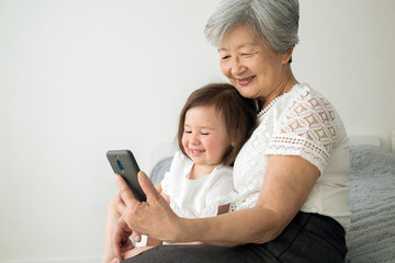 Great-grandmother sits with great-granddaughter and looks into the smartphone. Grandmother and granddaughter take a selfie on a smartphone. Grandmother with her granddaughter look into the phone