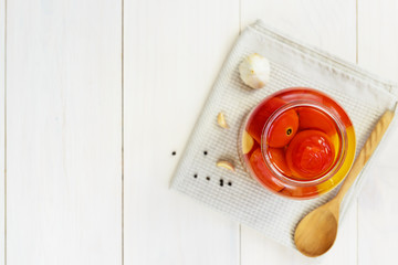 Marinated tomatoes in a jar on a white wooden table. Fermented vegetables, copy space, top view