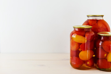 Marinated tomatoes in a jar on a wooden table. Light background, horizontal orientation, copy space.