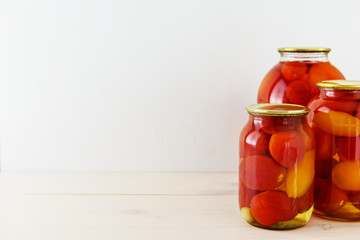 Marinated tomatoes in a jar on a wooden table. Light background, horizontal orientation, copy space.