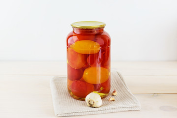 Marinated tomatoes in a jar on a light wooden table