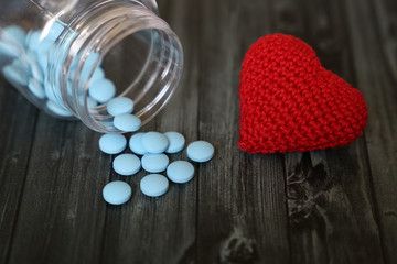 Blue pills and red knitted heart on dark wooden table. Concept for antidepressants, hypertension,...
