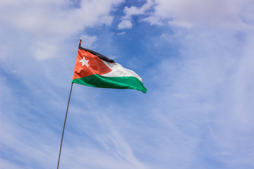 Jordanian Middle East country flag evolving in the wind, sign and symbols concept picture on blue sky with high white clouds background, copy space