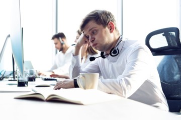 Worried or tired business man with headset working on computer in office.