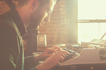 Vintage styled portrait of joung journalist typing on an antique vintage typewriter machine