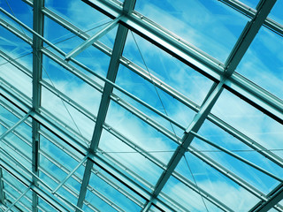 Transparent roof made of metal and glass with a blue sky with clouds visible through it.