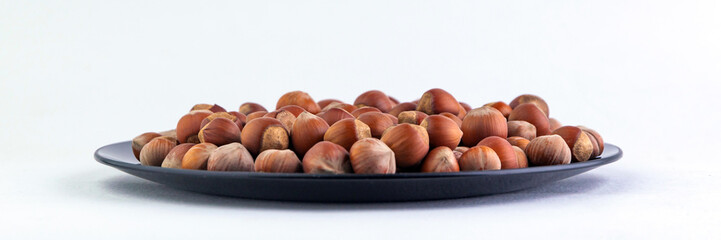 hazelnuts: many nuts lie on a black plate, on a white background