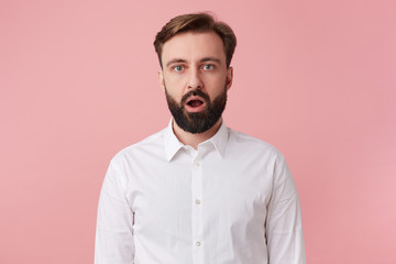 Photo of surprised young handsome bearded man who was told the secret, wearing a white shirt....