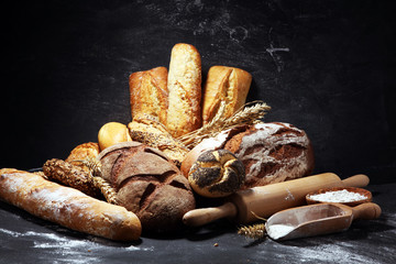 Assortment of baked bread and bread rolls on rustic black bakery table background