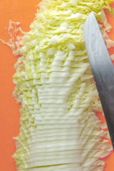 finely chopped Chinese cabbage on an orange board, a sharp knife next. Short focus, close