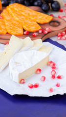 Different types of cheese and fruit. Sliced camembert and pomegranate. Soft and hard cheese and nuts. Camembert and grapes on blue background. Vegetarian food