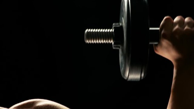 Man building muscles close up. Detail of young bodybuilder lifting weight on dark background. Lifting dumbbells for bigger biceps.