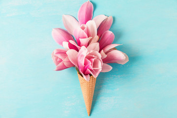 Ice cream of pink magnolia flowers in waffle cone on pastel colored blue background. flat lay. top...