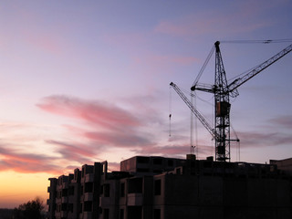 Construction of a multi-storey building with a crane on the background of a colorful sunset