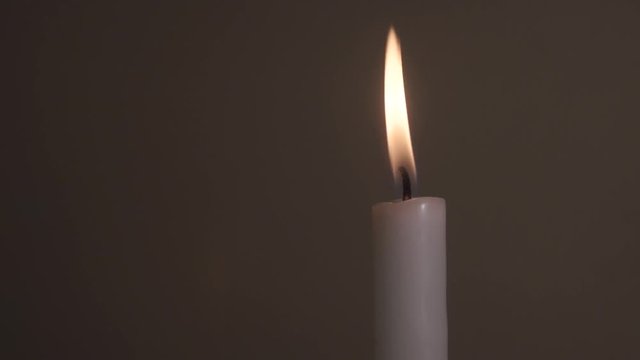 A single white candle flame being disturbed by a wind, isolated, close up
