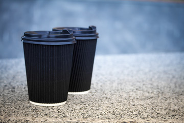 Two black disposable cups of coffee with lids are standing on the stone parapet