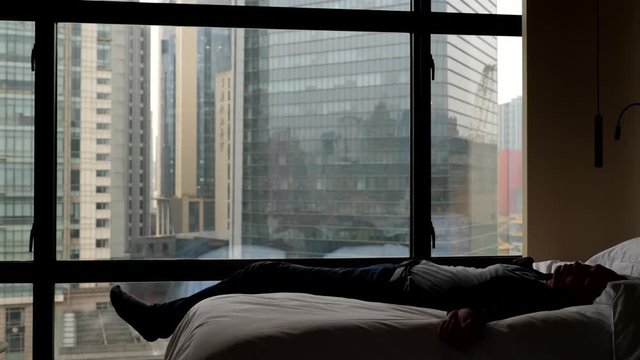 Man fall down on bed, need rest after hard work abroad. Dim bedroom at hotel with large window. Slow motion shot. Guy feel worn out and collapse on bed exhausted