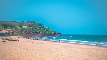 North Goa, India Candolim beach with Aguada fort in the background. Famous tourist summer vacations destination on the beach by Arabian Sea in Goa tropical climate with coconut palms.