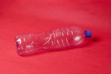Plastic empty bottle on a red background with space for text. Concept of environmental pollution by polyethylene waste