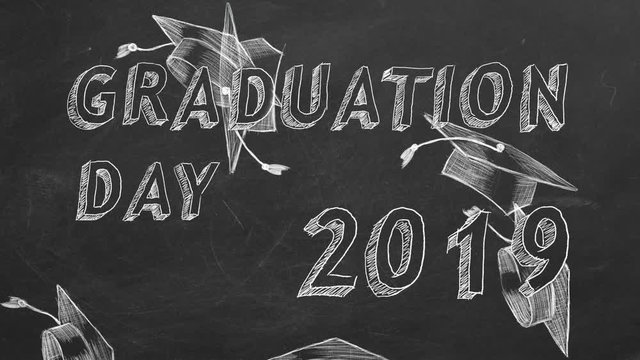 Hand drawing text "Graduation day. 2019." and graduation caps on blackboard.