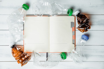Plastic bottles on a background of a notebook with blank pages. Concept of caring for environment, recycling. Secondary plastic circuit. Environment pollution. Entering information about recycling.