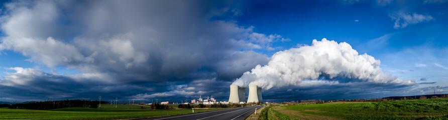 Nuclear plant and its cooling towers releasing a huge cloud of steam to the sky. Verdant vegetation...