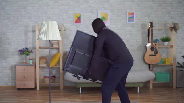 anonymous thief in a Balaclava mask stealing TV in the house and experiencing back pain injury