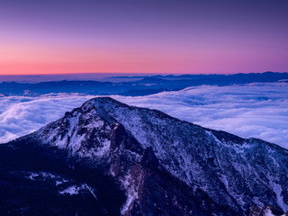 山頂より夜明け前の風景、山々は雪景色で雲海に包まれ、空は夜明けのピンク色に染り始めた。