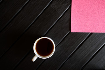 Cup of tea and pink napkin on a black wooden table. View from above. Minimalism