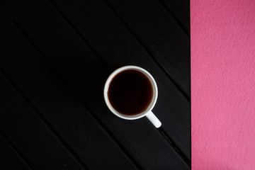 A cup of black tea and a pink napkin on a dark wooden table. View from above. Minimalism