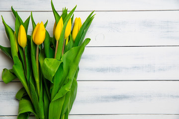Top view of yellow tulips on a wooden table. The concept of handing flowers to a woman, girl. Beautiful tulips and flowers, mother's day, women's day.