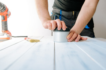 The man unscrews the paint can. The concept of DIY and renovation of new things. A man tinkering at home, working with wood.