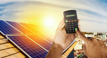 Holding a calculator on a solar panel photovoltaic installation in the background.