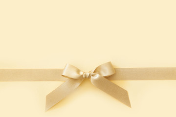 Gold ribbon with a bow as a gift on a beige background