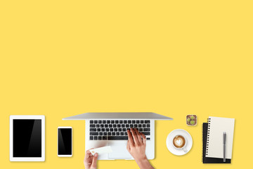technology working table with woman hands on laptop computer, credit card, coffee cup and cell phone on yellow background (or shopping and payment online concept)