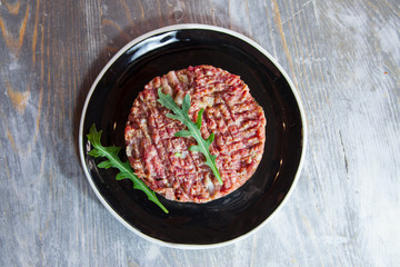 Steak tartare, cut and sliced with a knife, made of ground minced beef, on display on a rustic wooden table. Steak tartare is a symbolic dish of the French gastronomy made of ground raw meat