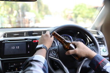 man driving car and holding alcohol bottle in another hand while on the road