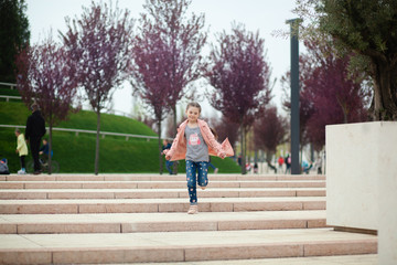 Obraz premium cute pretty girl 7-8 years old in a pink raincoat in the park in spring