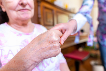 A young woman is holding the hand of an old woman