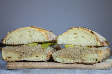 Liver Pate sanwdich in a French baguette sliced in two, made of duck and chicken Pate de Foie with some sliced pickles, on display on a rustic wooden table. It is a typical French snack
